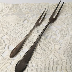 May include: Two silver cake forks on a white crocheted doily.