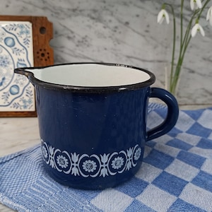 Könnte beinhalten: Ein blauer Emaille-Krug mit einem weißen Blumenmuster am Rand. Der Krug hat ein weißes Innenleben und einen schwarzen Rand.