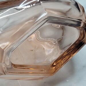 May include: A clear glass bottle with a pink tint and a faceted design. The bottle is empty and has a smooth, rounded bottom.