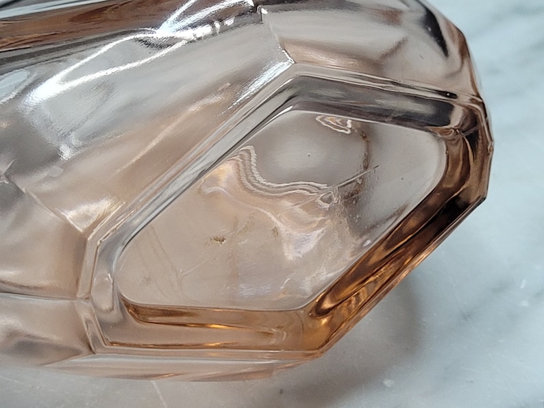 May include: A clear glass bottle with a pink tint and a faceted design. The bottle is empty and has a smooth, rounded bottom.