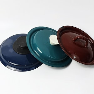 Może przedstawiać: Trzy pokrywki do garnków w różnych kolorach: niebieskim, turkusowym i bordowym. Pokrywki mają biały guzik na górze i uchwyt na bordowej pokrywce.