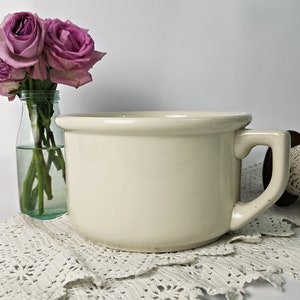 Könnte beinhalten: Eine weiße Keramik-Toilette mit einem einzigen Griff. Die Toilette steht auf einer weißen Häkelspitze. Im Hintergrund steht eine Vase mit rosa Rosen.