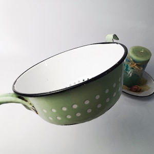 May include: A green enamel colander with white polka dots and a black rim. The colander has a handle and a strainer.