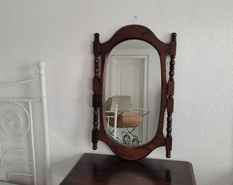 Peut inclure: Un miroir de toilette en bois foncé avec un miroir ovale et des moulures en bois décoratives. Le miroir reflète une chaise blanche avec un siège en osier.