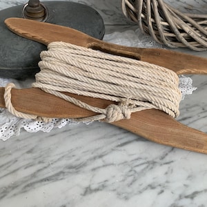 Op de afbeelding: Een houten touwopwinder met een natuurlijke afwerking. De opwinder heeft twee armen die omhoog buigen en in het midden samenkomen. Een spoel met wit touw is om de armen gewikkeld.