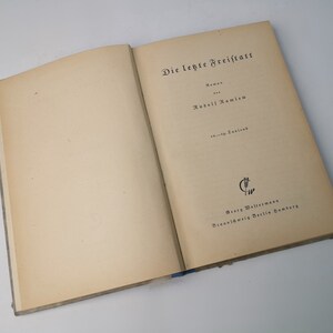 May include: An open book with the title "Die letzte Freitags" by author "Rudolf Ramlow" printed on the cover. The book is published by "Georg  Westermann" in "Braunschweig, Berlin, Hamburg".