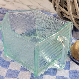 Könnte beinhalten: Eine klare Glasschale mit strukturierter Oberfläche und einem Griff. Die Schale ist sechseckig und hat eine leicht mattierte Optik.