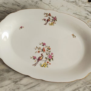 Könnte beinhalten: Weiße ovale Servierplatte mit goldfarbenem Rand und einem Blumendesign mit rosa, gelben und roten Blumen und zwei Vögeln.