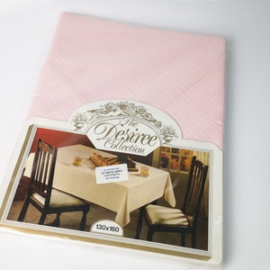 May include: A pink tablecloth with a white stripe pattern. The tablecloth is packaged with a picture of a table setting with two chairs, a white tablecloth, and a chessboard. The packaging also includes the text "The Desiree Collection" and "130x160".
