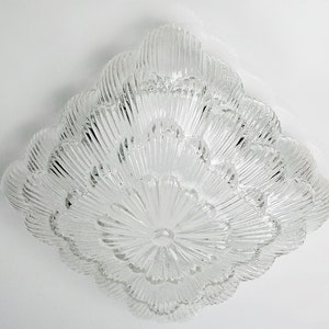 May include: A clear glass ceiling light fixture with a layered, flower-like design. The light fixture has a circular shape and is made of many small, clear glass pieces.