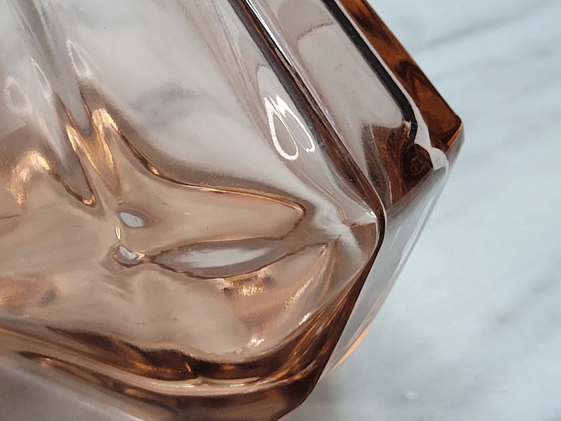 May include: A close-up of a clear glass vase with a textured surface. The vase is a light pink colour and has a square shape.