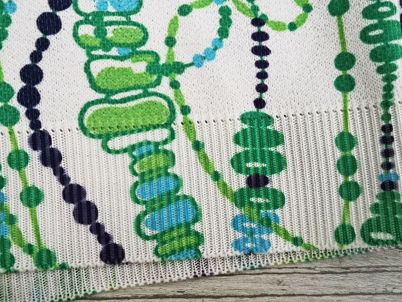 May include: White fabric with a green, blue, and black abstract pattern. The pattern features circles, lines, and shapes.