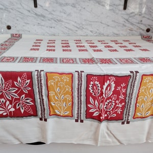 May include: White tablecloth with a red, yellow, and brown floral pattern. The tablecloth has a repeating pattern of squares with a floral design in each square.