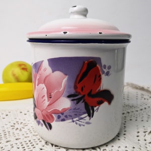 Könnte beinhalten: Weiße Emaille-Dose mit rosa Deckel und einem Blumendesign mit rosa, roten und violetten Blumen. Die Dose hat einen blauen Rand.