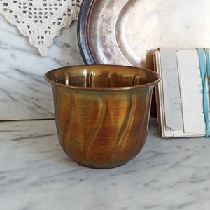 Può includere: Un piccolo vaso in ottone con una superficie ondulata e testurizzata. Il vaso è di un colore marrone dorato caldo.