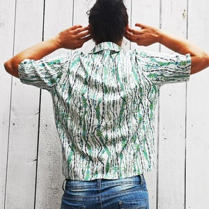 May include: A white short-sleeved shirt with a green and black patterned design. The pattern features a series of lines and dots.