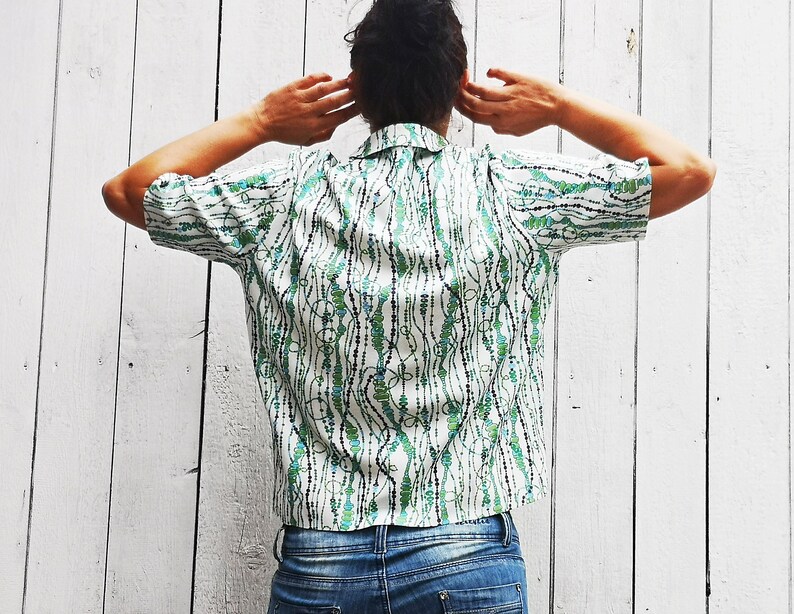 May include: A white short-sleeved shirt with a green and black patterned design. The pattern features a series of lines and dots.