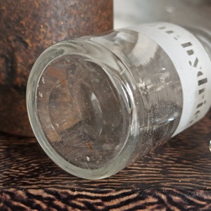May include: A clear glass bottle with a white label that says "India" on it. The bottle is lying on a brown surface.