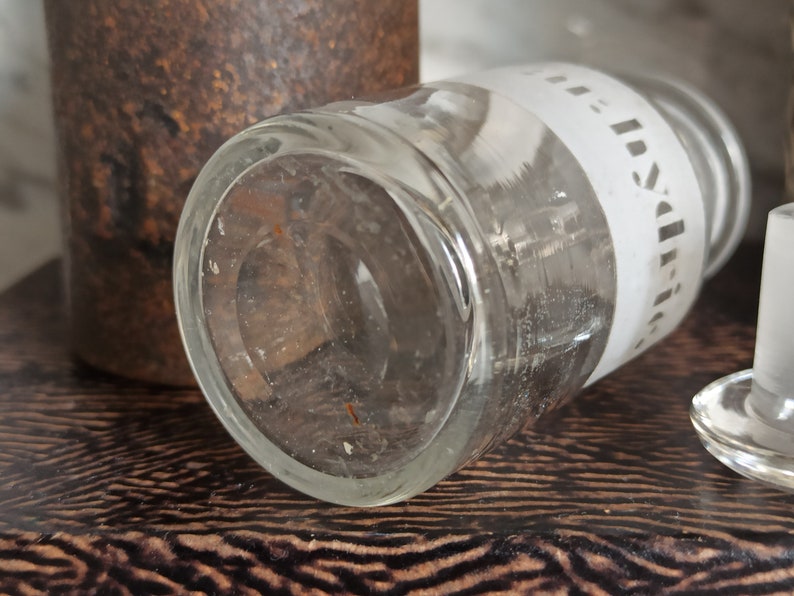 May include: A clear glass bottle with a white label that says "India" on it. The bottle is lying on a brown surface.