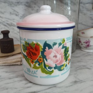 Könnte beinhalten: Weiße Emaille-Dose mit rosa Deckel und blauem Rand. Die Dose hat ein Blumenmuster mit rosa, roten und grünen Blumen.