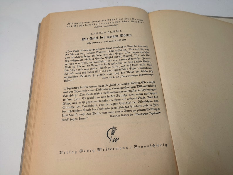 May include: A vintage book titled "Die Infel der wei&szlig;en G&ouml;ttin" by Carola Schiel. The book cover features a decorative design with a wheat stalk symbol and the text "Verlag Georg Westermann / Braunschweig".
