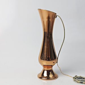 Könnte beinhalten: Eine Kupfervase mit einem Messinggriff. Die Vase hat einen runden Körper und einen ausgestellten Boden. Es ist eine kleine Vase, etwa 25 cm hoch.