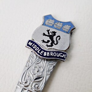 May include: Silver-toned letter opener with a decorative floral design and a shield-shaped emblem. The emblem features a black lion, three blue ships, and the word "MIDDLESBROUGH" in blue lettering.