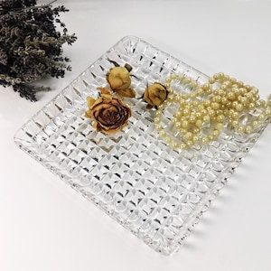 Può includere: Un vassoio da portata in vetro trasparente con un motivo a diamante. Il vassoio è decorato con fiori secchi e una collana di perle.