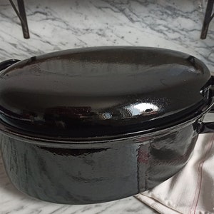 May include: Black enameled cast iron oval Dutch oven with a lid. The oven has two handles on each side and a shiny black finish.