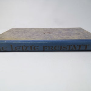 May include: A blue hardcover book with the title "Die letzte Freistatt" printed in gold lettering on the spine.