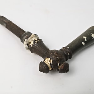 May include: A vintage door handle with a long, thin metal shaft and two wooden knobs. The knobs are dark brown with white paint accents. The handle is in a worn condition, showing signs of age and use.