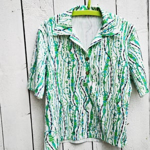 May include: A white short-sleeved shirt with a green and blue abstract pattern. The shirt has a collared neckline and a button closure.