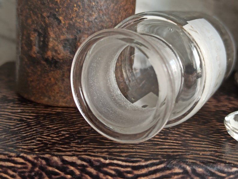 May include: A clear glass bottle with a frosted rim and a white label. The bottle is sitting on a dark wooden surface.