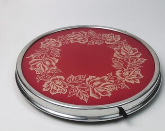 May include: A red and silver round serving tray with a decorative floral design of roses in a wreath pattern.