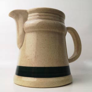 Peut inclure: Un pichet en céramique beige avec une bande verte autour du bas. Le pichet a un corps arrondi et une poignée.