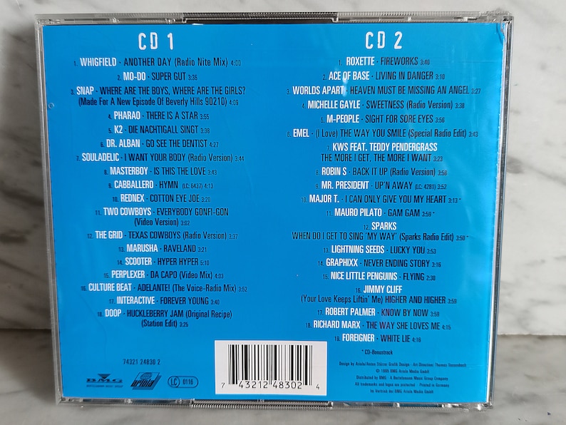 May include: A blue CD case with a white border and a list of songs on each side. The front of the case has the title "CD 1" and "CD 2" printed in white. The back of the case has a barcode and the text "7 43212 48302 4".