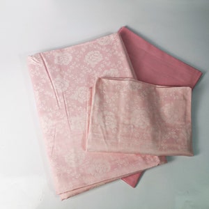 May include: A set of pink and light pink fabric with a white floral pattern. The fabric is folded and stacked on a white surface.