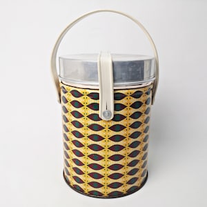 May include: A vintage yellow, green, and maroon patterned metal lunch pail with a white handle and a silver lid.