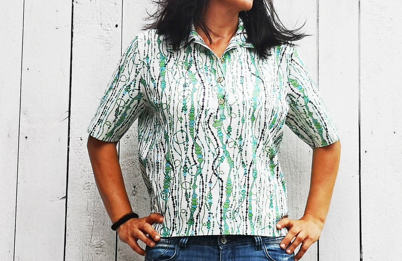 May include: A white short-sleeved shirt with a green and blue abstract pattern. The shirt has a collar and a button closure.