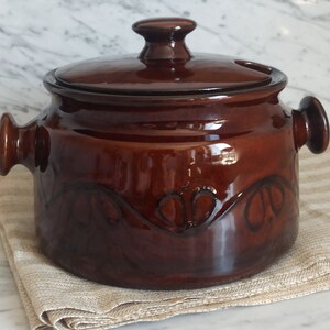 May include: A brown ceramic soup tureen with a lid and two handles. The tureen has a decorative design on the side.