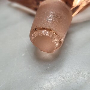 May include: Close-up of a clear glass bottle stopper with a gold rim. The stopper has a slightly chipped edge.