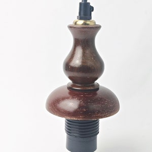 May include: A wooden lampshade with a dark brown finish. The lampshade has a round base and a bulbous top. The lampshade is attached to a black electrical cord.