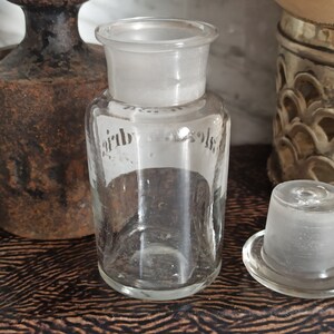 May include: A clear glass bottle with a frosted glass stopper. The bottle has a label with the word "Air" on it.