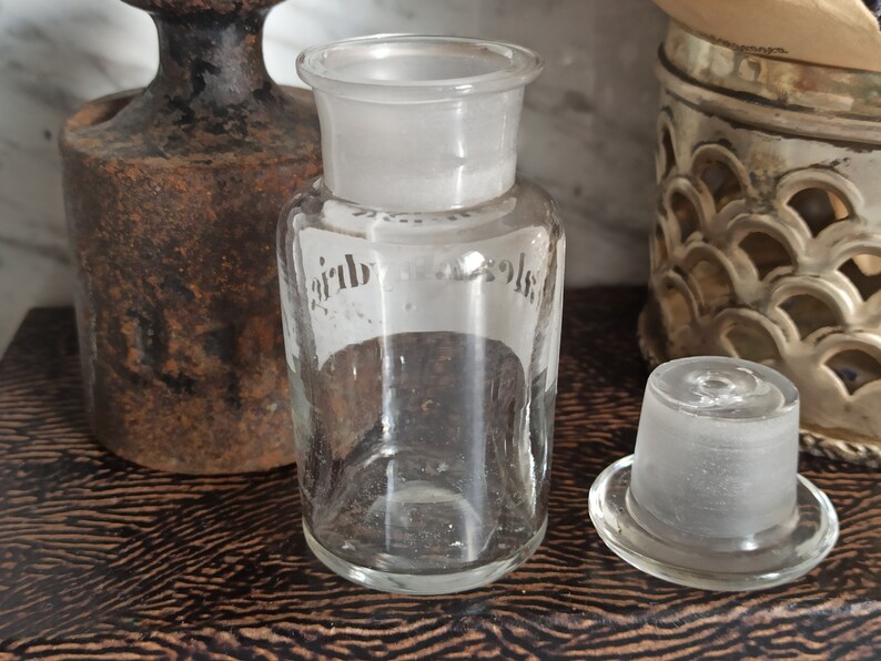 May include: A clear glass bottle with a frosted glass stopper. The bottle has a label with the word "Air" on it.