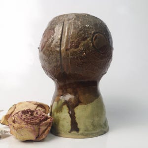 Könnte beinhalten: Eine kleine, braune Keramikvase mit einer strukturierten Oberfläche und einer grünen Glasur. Die Vase hat eine abgerundete Oberseite und einen breiten Boden.