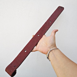 May include: A long, rusty red metal hinge with rounded ends and four holes. The hinge is about 30 inches long.
