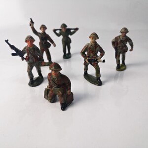 Peut inclure: Un ensemble de six soldats de jouet en uniforme de camouflage. Les soldats tiennent des fusils et sont debout sur une surface blanche.