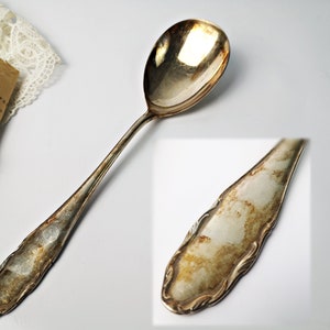 May include: A silver spoon with an ornate handle and a rounded bowl. The spoon has a worn, aged appearance.
