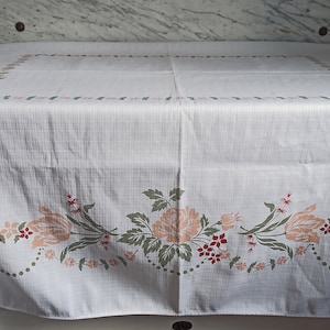 Könnte beinhalten: Weiße Tischdecke mit einem floralen Muster in Rosa-, Grün- und Rottönen. Das Muster zeigt stilisierte Blumen und Blätter.