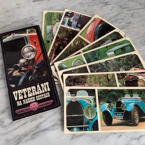 May include: A collection of vintage car postcards, fanned out on a marble surface. The postcards feature classic car images, with a box displaying the text "VETERÁNI NA NAŠICH CESTÁCH" in white and pink.